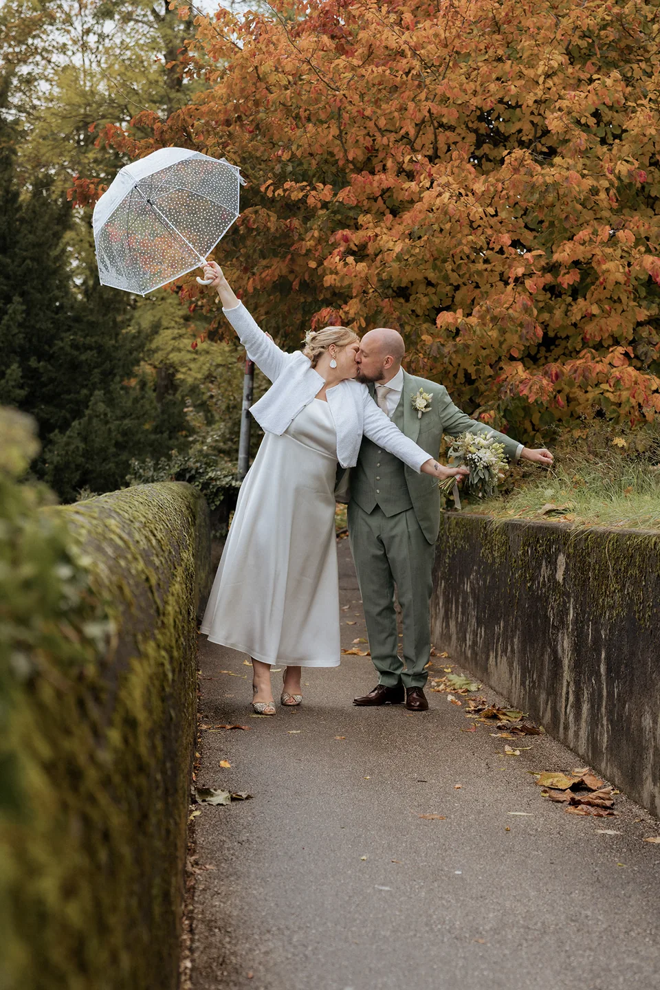 Les mariés s’embrassent sous un parapluie en automne