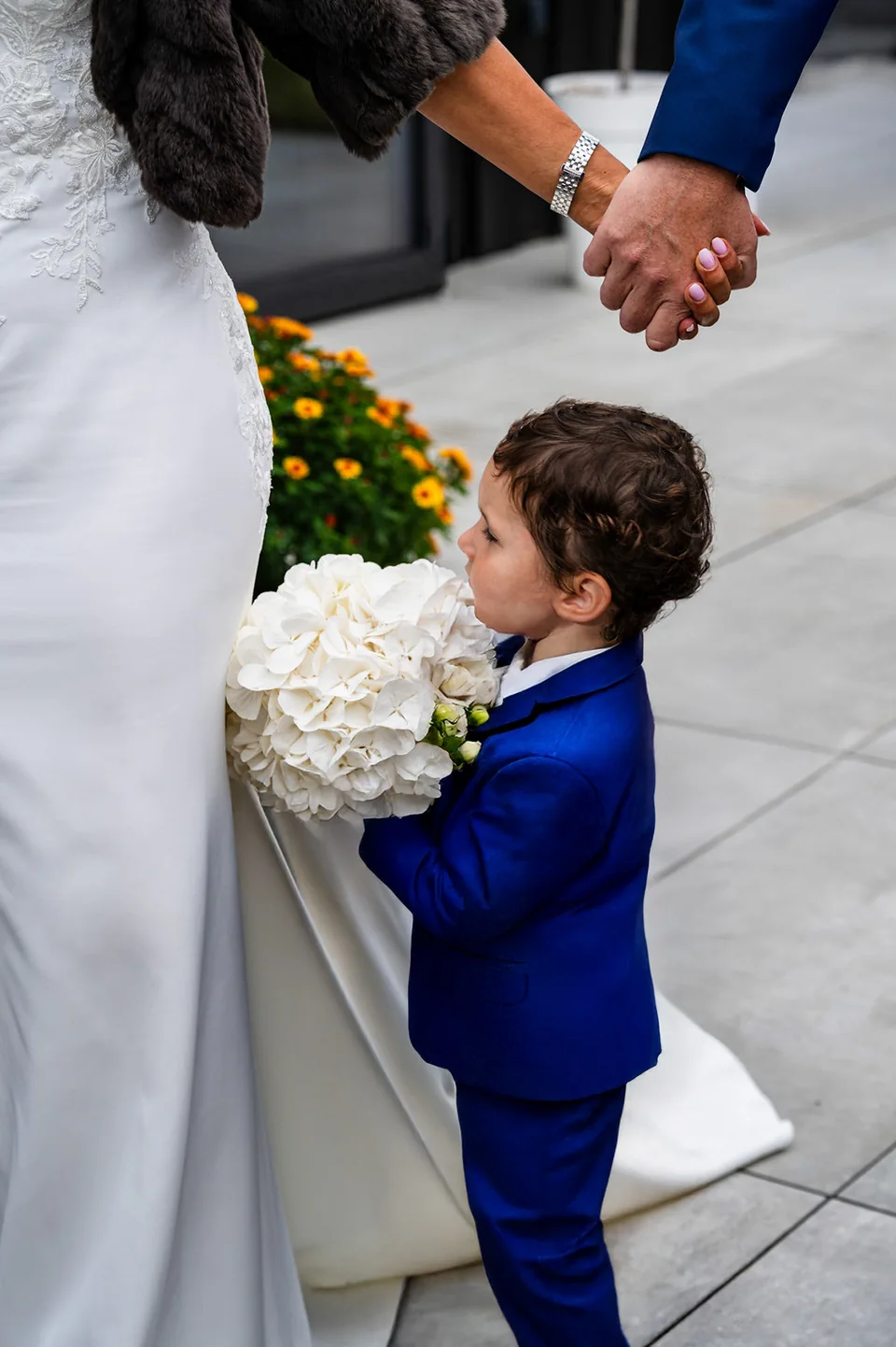 Un enfant en costume bleu tient le bouquet près des mariés