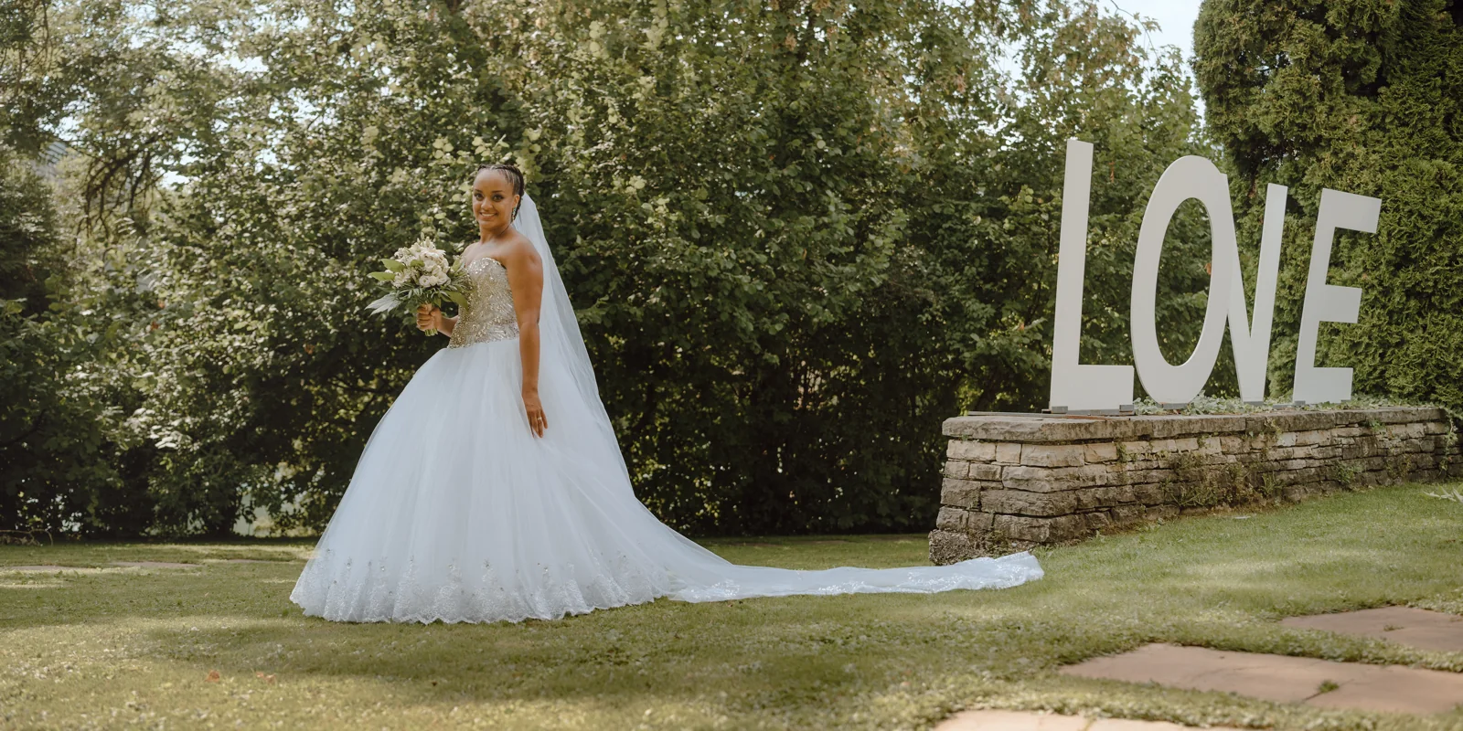 Mariée en robe blanche dans un jardin devant les lettres LOVE
